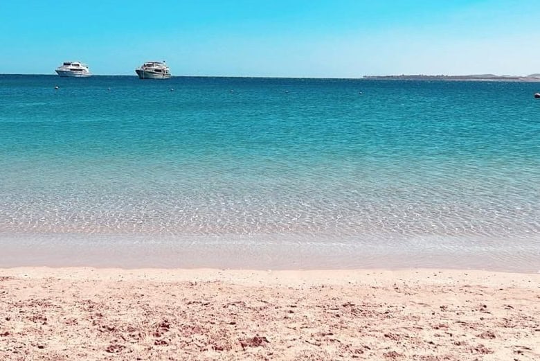 Beach with turquoise water, sandy shore, and boats on the horizon.