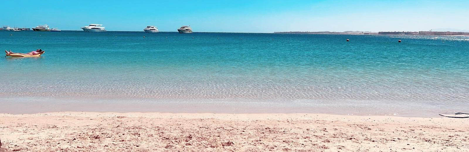 Beach with turquoise water, sandy shore, and boats on the horizon.