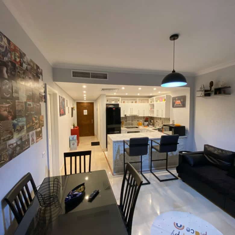 Spacious living room with dining table, black sofa, and kitchen in the background.