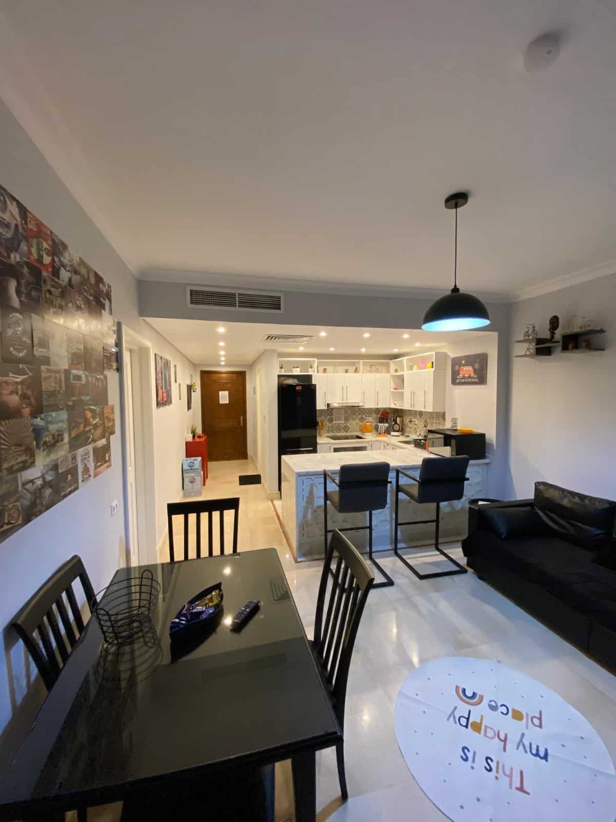 Spacious living room with dining table, black sofa, and kitchen in the background.