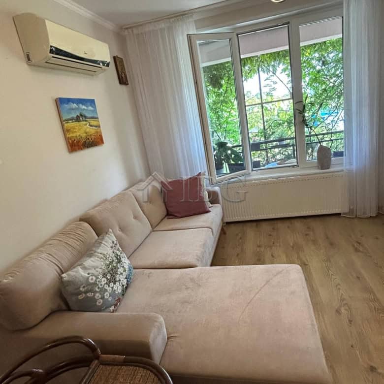 Bright living room with a large window overlooking greenery, featuring a comfortable beige sofa and.
