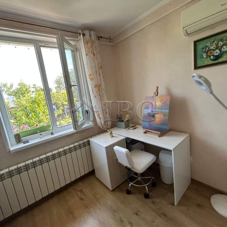 Bright home office with a desk, chair, and artwork near a large window in a quiet area.