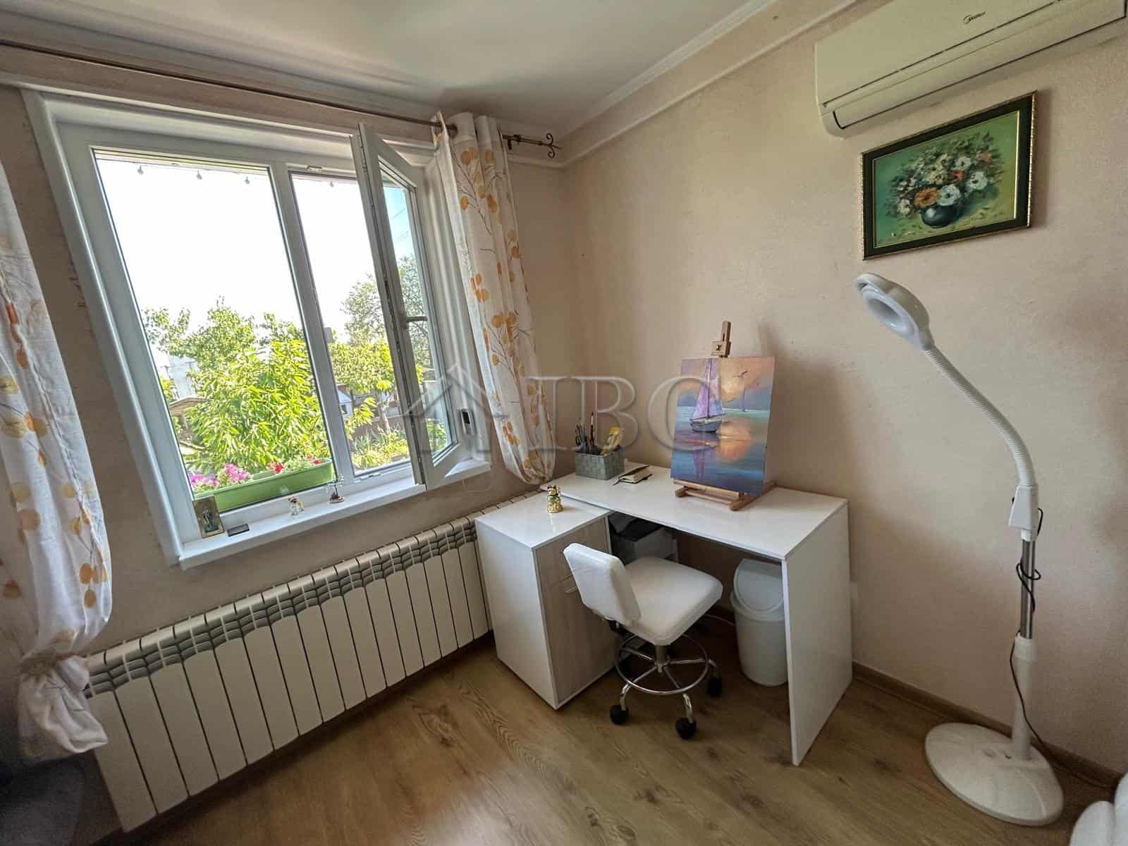 Bright home office with a desk, chair, and artwork near a large window in a quiet area.