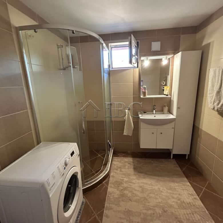 Bright bathroom with shower, washing machine, and vanity in a quiet residential area.