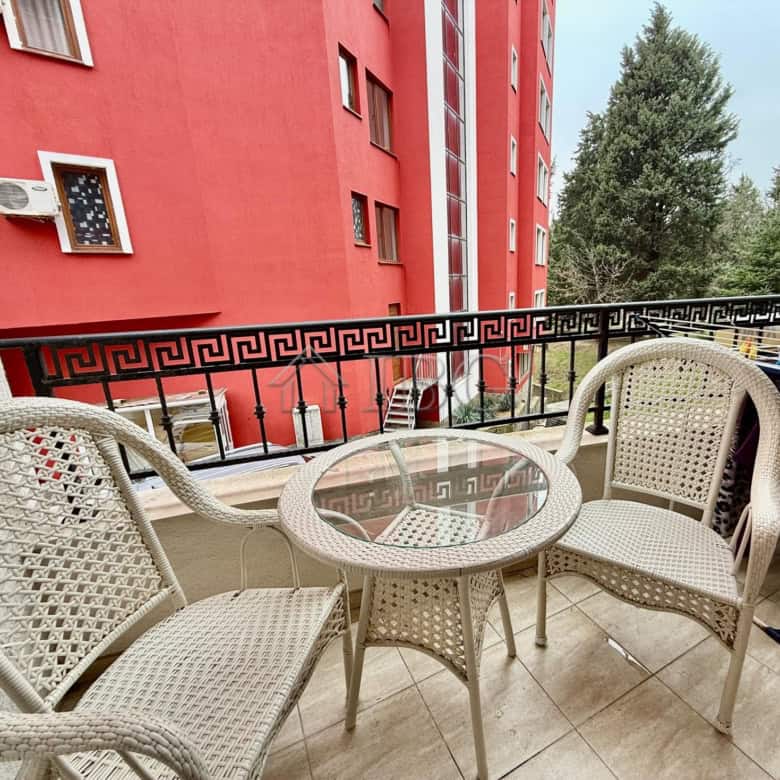 Balcony with wicker chairs and glass table overlooking Nessebar's vibrant cityscape. Perfect for rel.