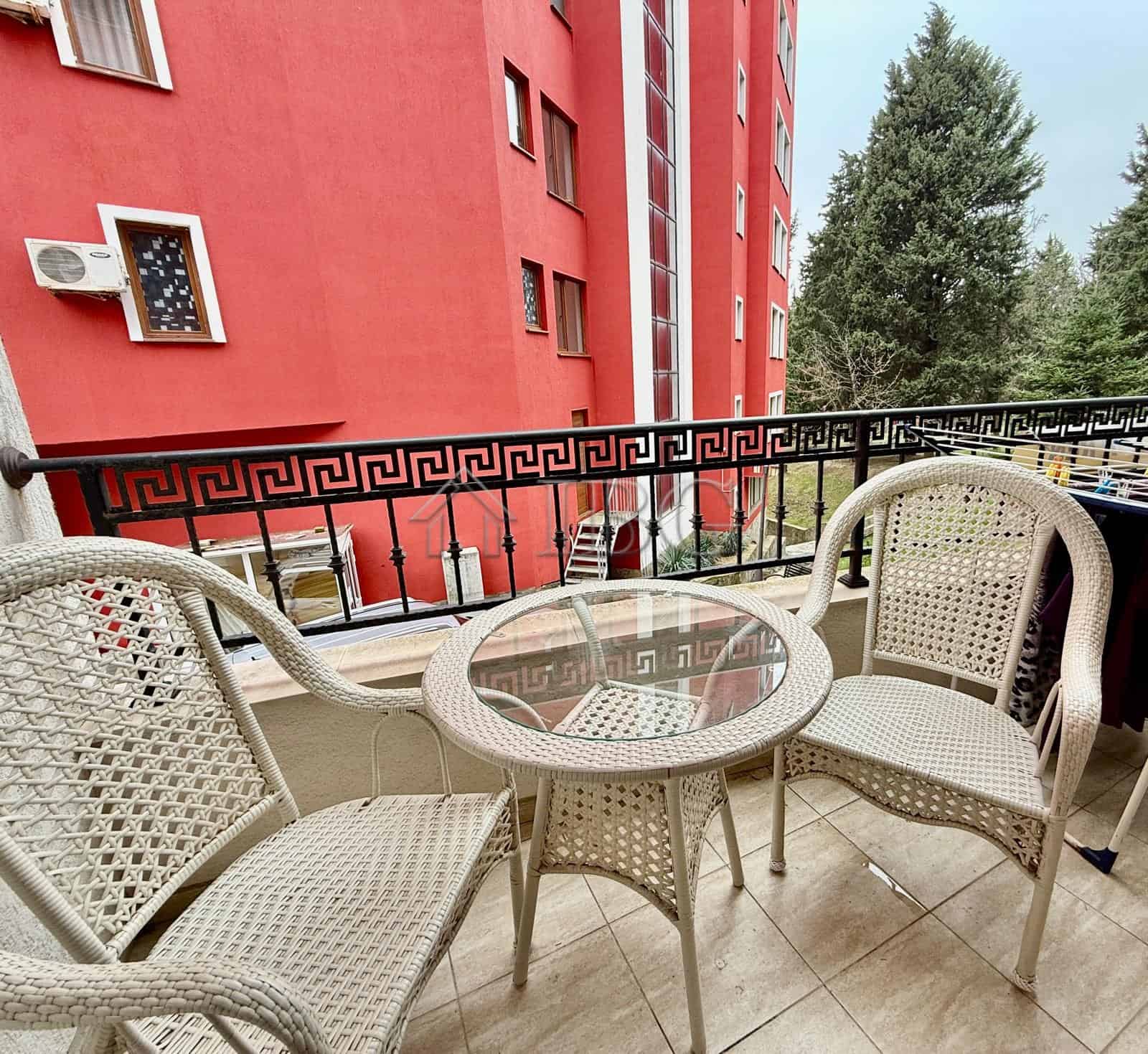 Balcony with wicker chairs and glass table overlooking Nessebar's vibrant cityscape. Perfect for rel.