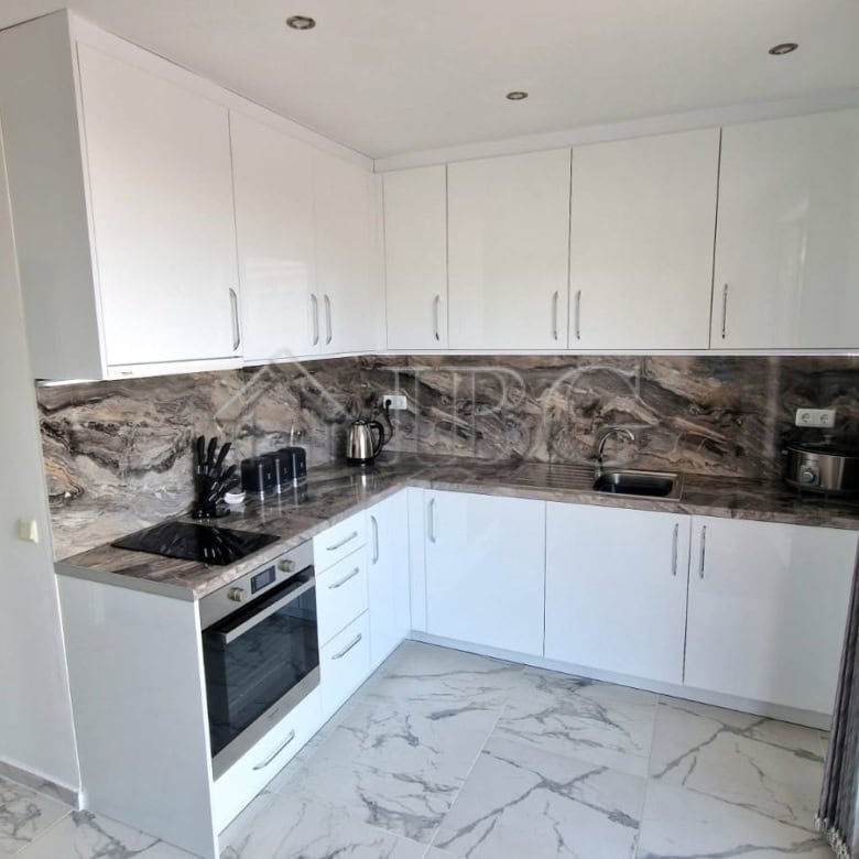 Modern white kitchen with marble countertops and large glass door opening to a balcony.
