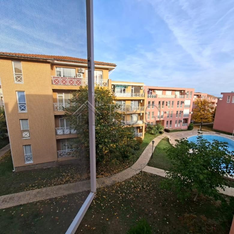 View of sunny beach apartment complex with pool and green spaces on a bright day.