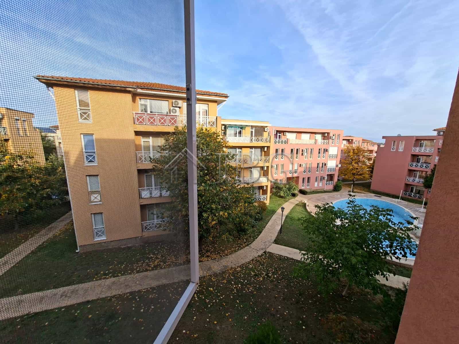 View of sunny beach apartment complex with pool and green spaces on a bright day.