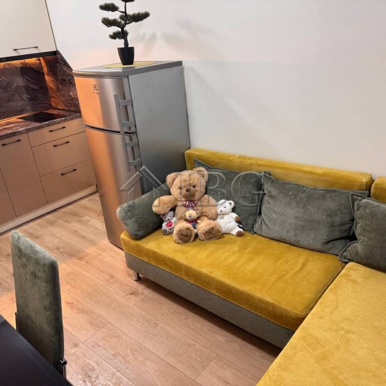 Interior of a 1-bedroom apartment with a pool view, featuring a yellow sofa and plush toys.