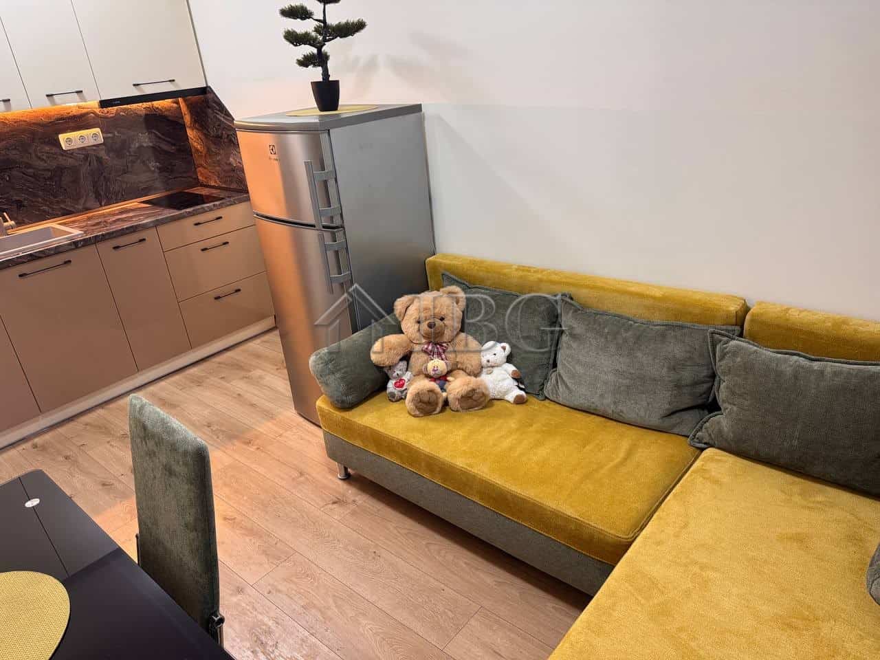 Interior of a 1-bedroom apartment with a pool view, featuring a yellow sofa and plush toys.