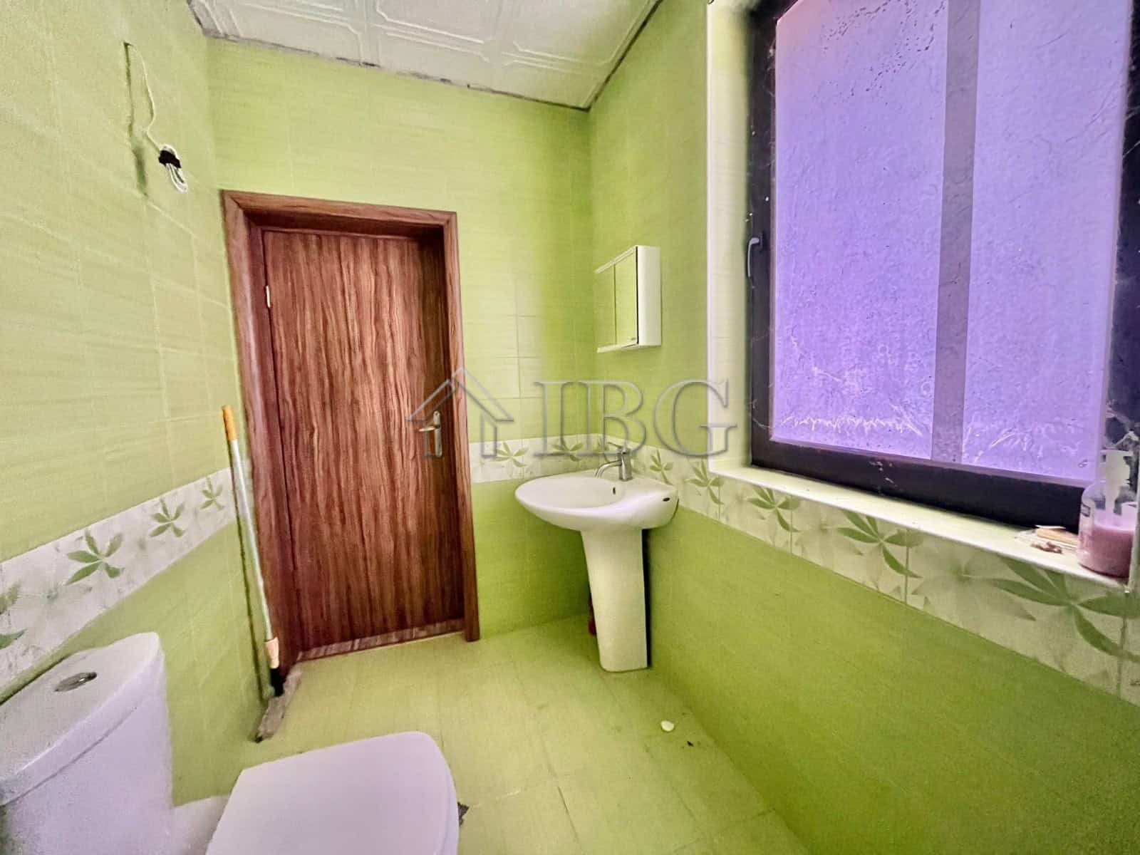 Bright bathroom with green walls, window, and white fixtures in Goritsa Village.