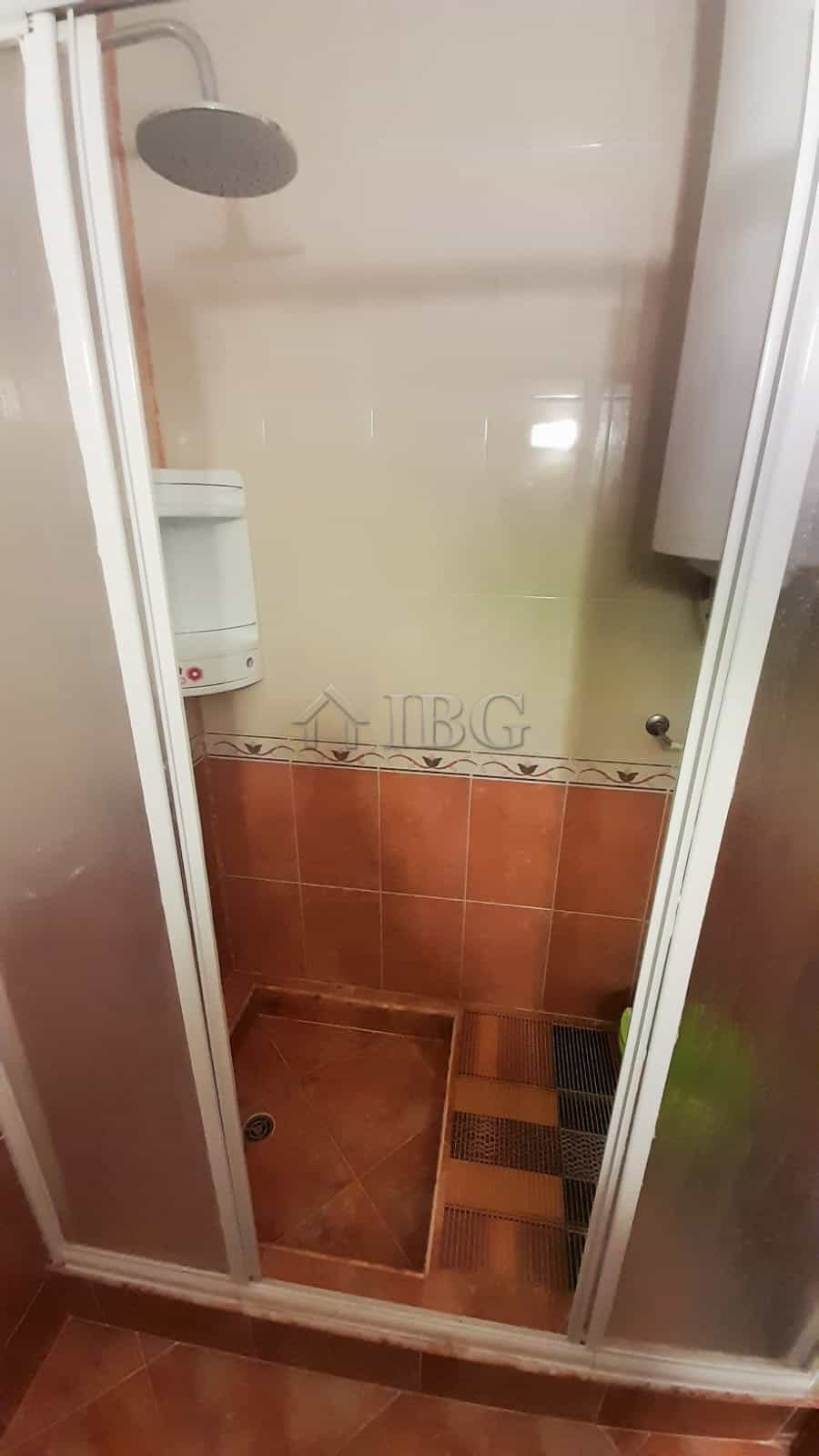 Shower stall with glass door and tiled interior in a small bathroom setting.