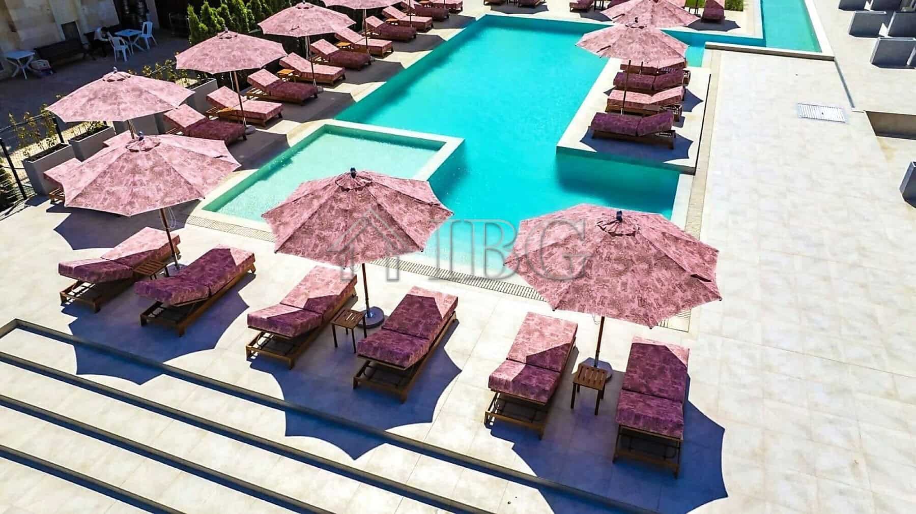 Pool area with pink sun loungers and umbrellas in a contemporary resort setting.