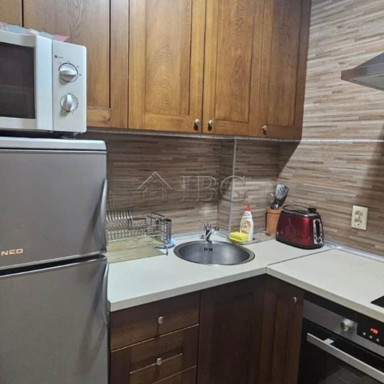 Kitchen with wooden cabinets, microwave, refrigerator, and cooking area in Ruse.