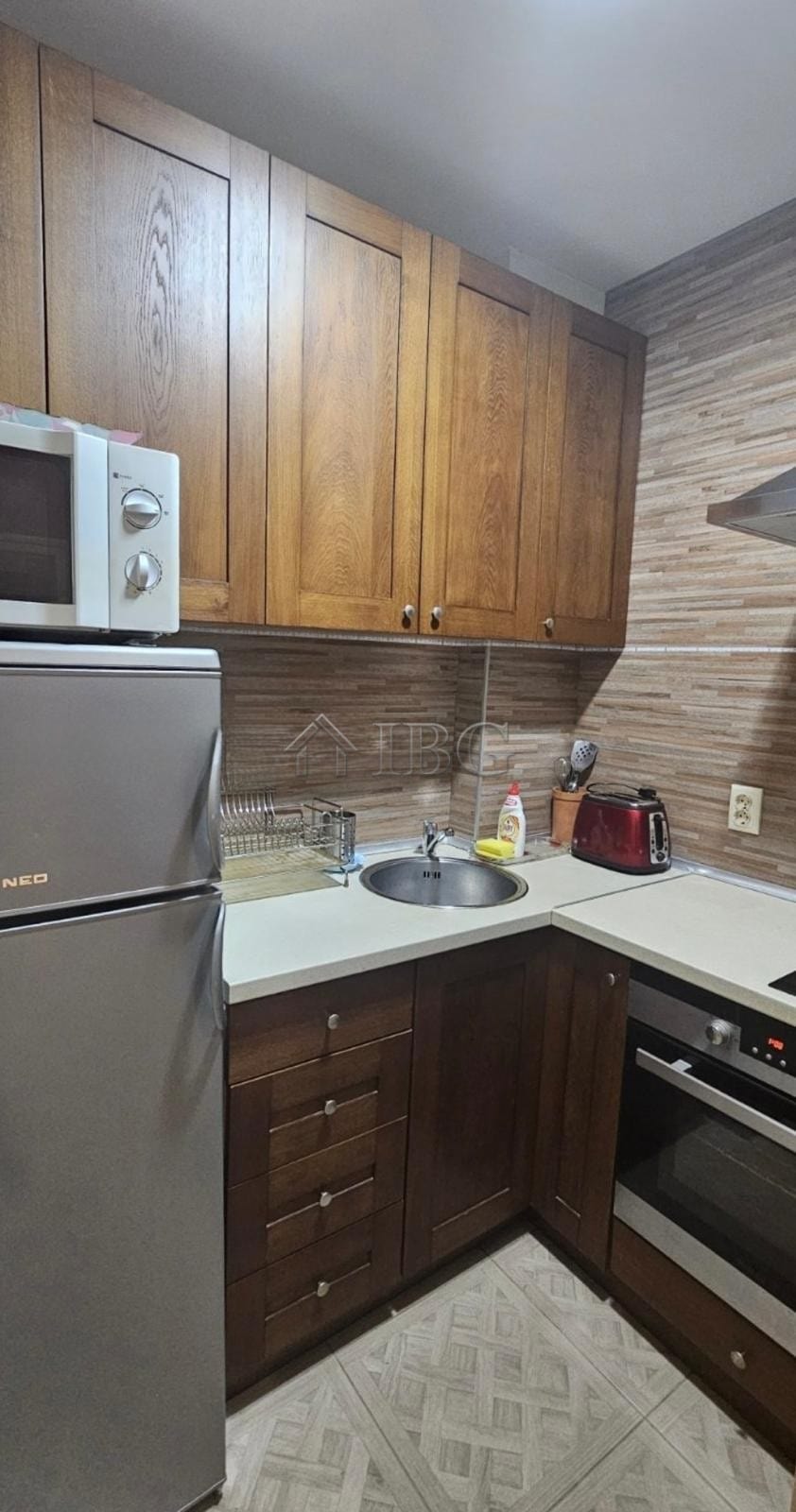 Kitchen with wooden cabinets, microwave, refrigerator, and cooking area in Ruse.