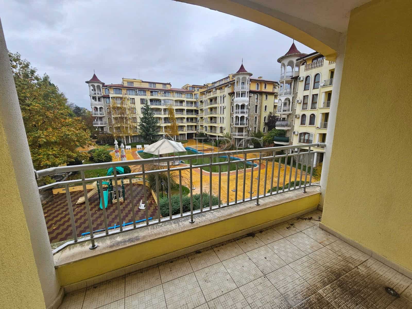 Balcony view of a two-bedroom apartment overlooking a swimming pool and residential complex.