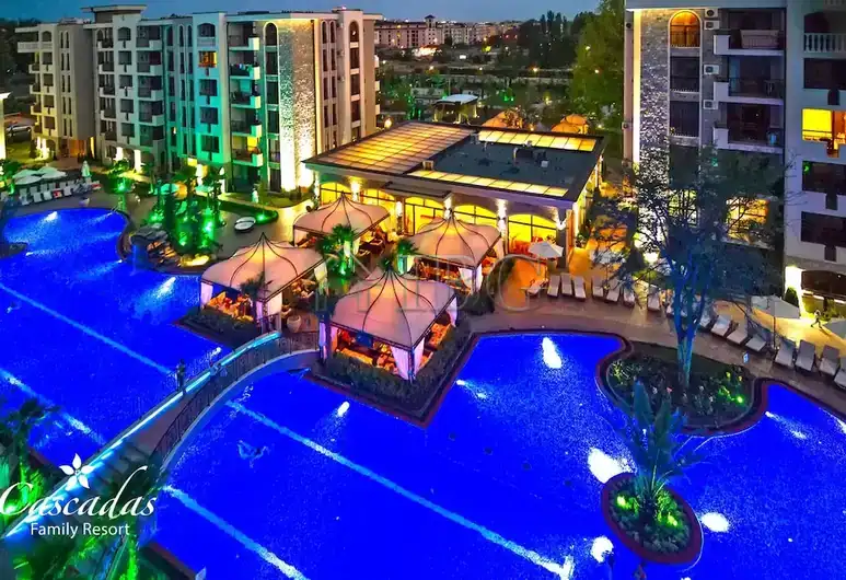 Bright night view of Cascadas Family Resort with illuminated pools and outdoor lounge areas.