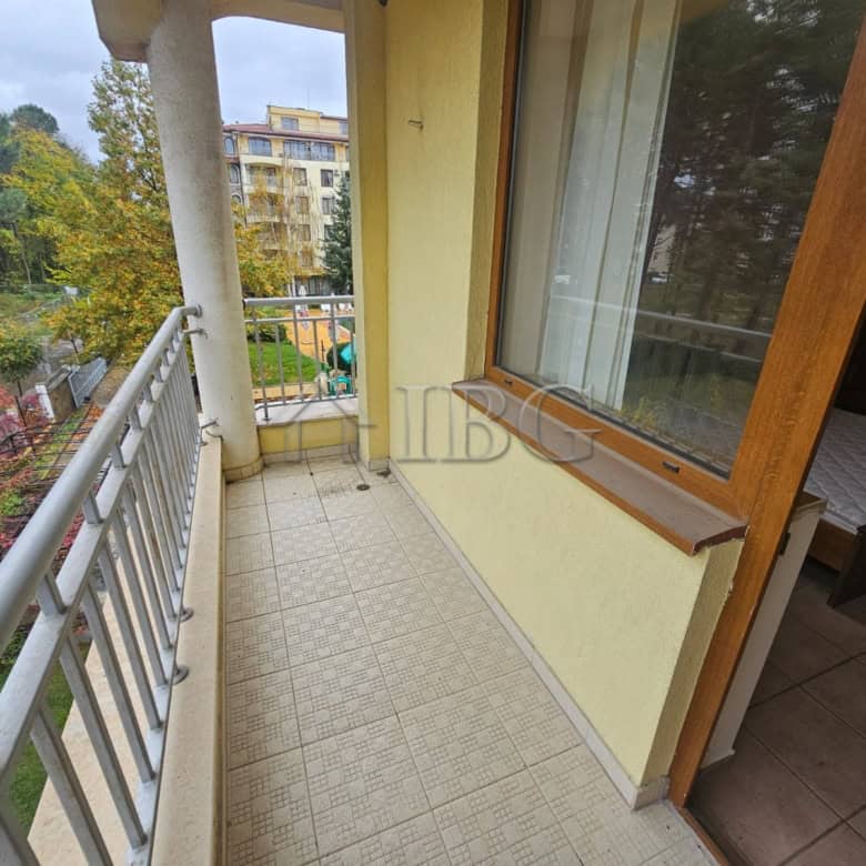 Balcony with railing overlooking pool area in a sunny beach apartment.
