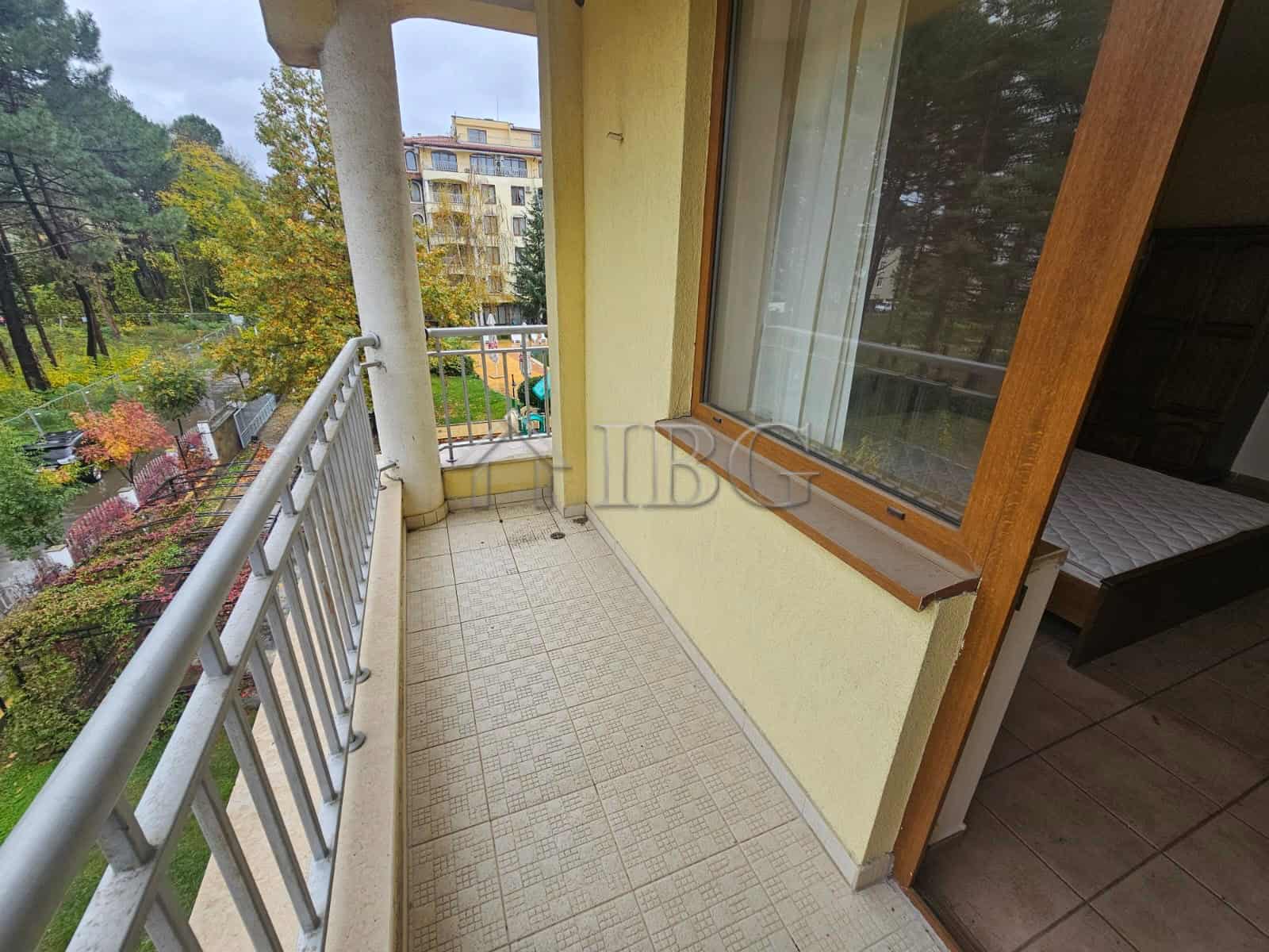 Balcony with railing overlooking pool area in a sunny beach apartment.
