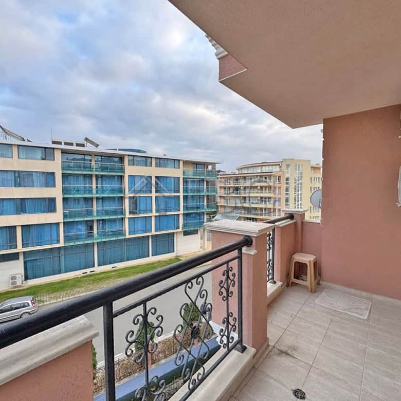Balcony view of a 1-bedroom apartment overlooking a pool and modern buildings in Sunny Beach.
