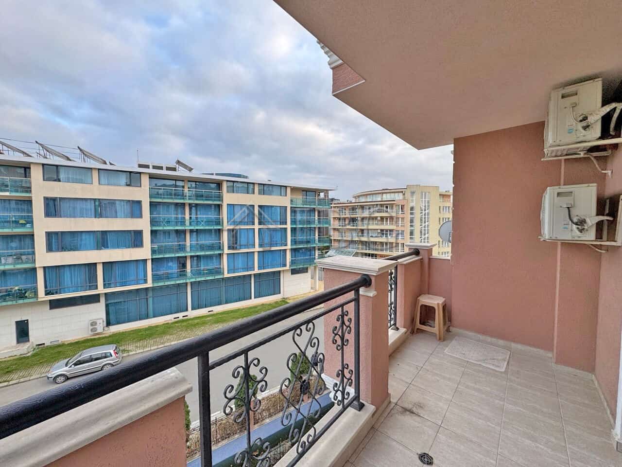 Balcony view of a 1-bedroom apartment overlooking a pool and modern buildings in Sunny Beach.