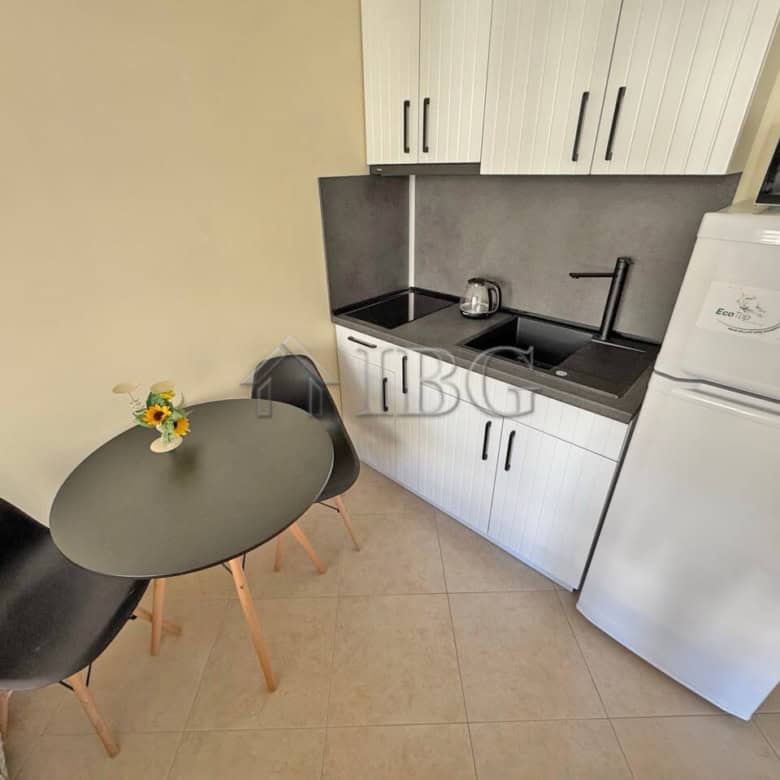 Compact kitchen with sink, cabinets, and washing machine in a sunny beach resort apartment.