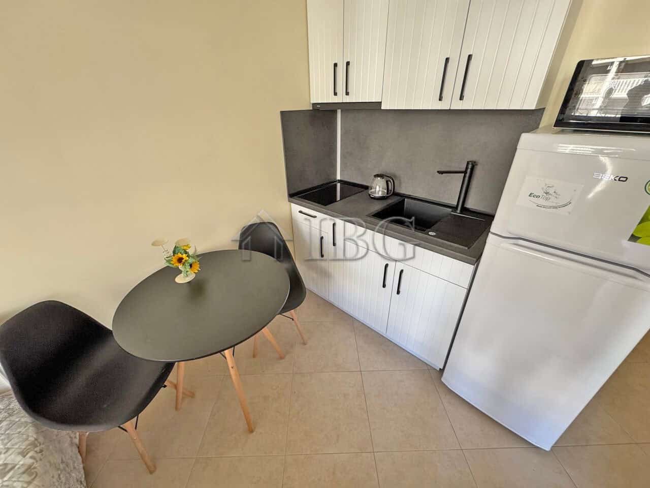 Compact kitchen with sink, cabinets, and washing machine in a sunny beach resort apartment.