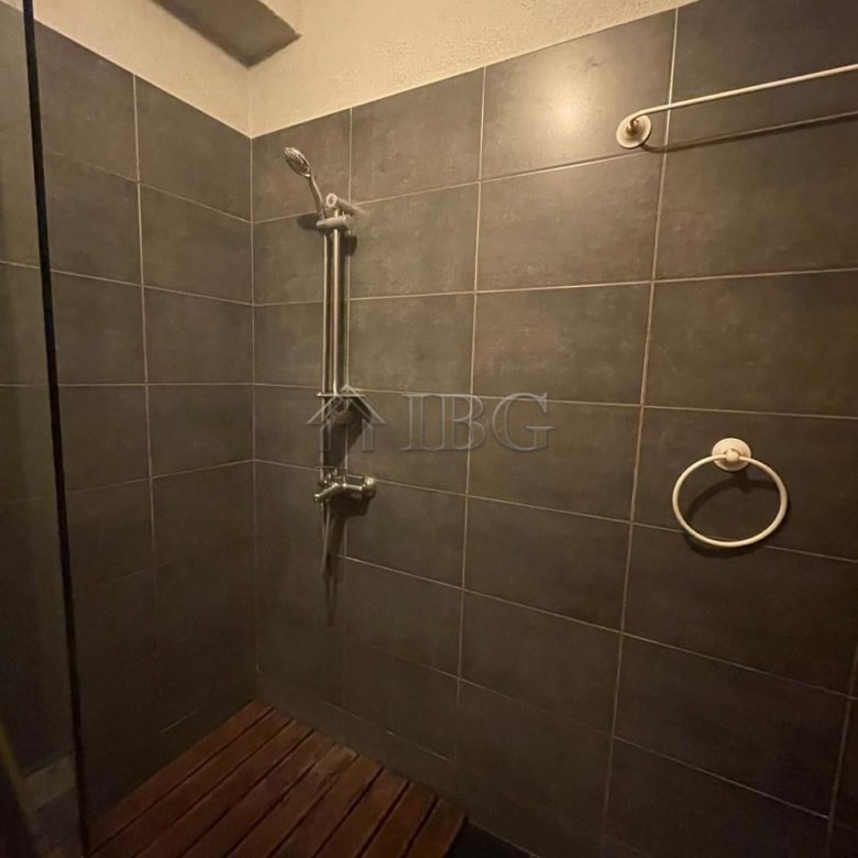 Shower area with modern fixtures and dark tiled walls in a sunny studio apartment.