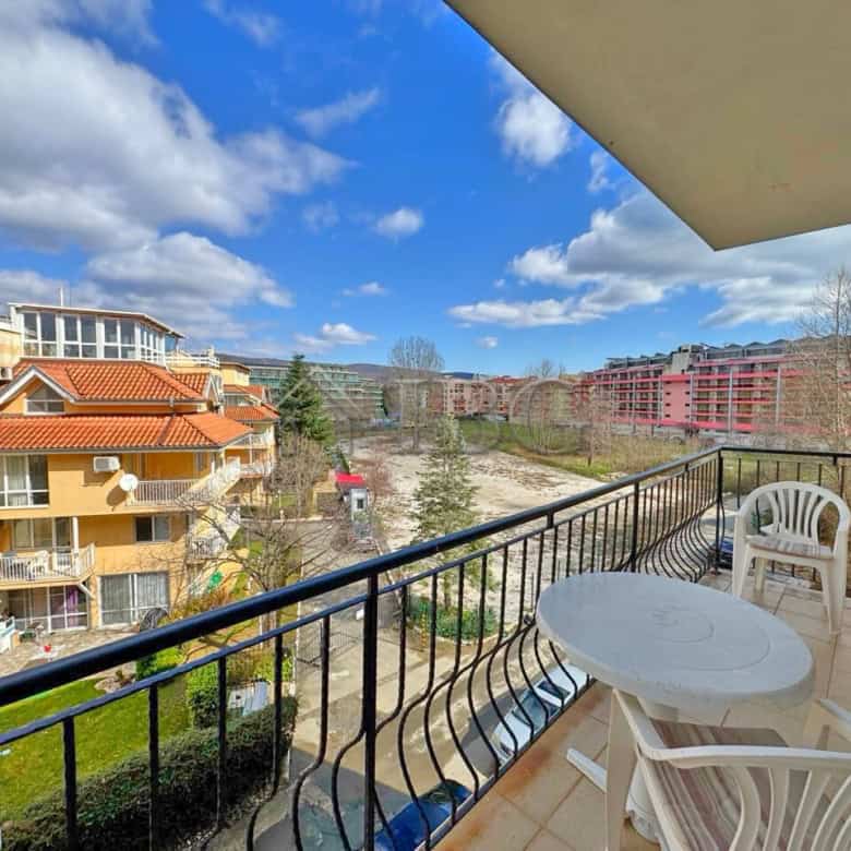 Balcony with outdoor seating overlooking residential buildings and green spaces in Sunny Beach.