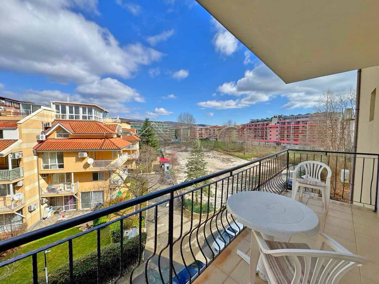 Balcony with outdoor seating overlooking residential buildings and green spaces in Sunny Beach.