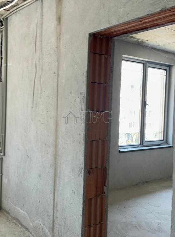 Unfinished apartment interior with window view and exposed brick doorway.