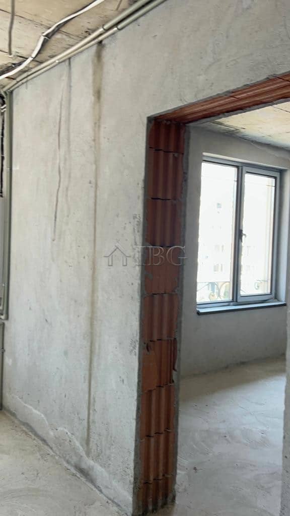 Unfinished apartment interior with window view and exposed brick doorway.