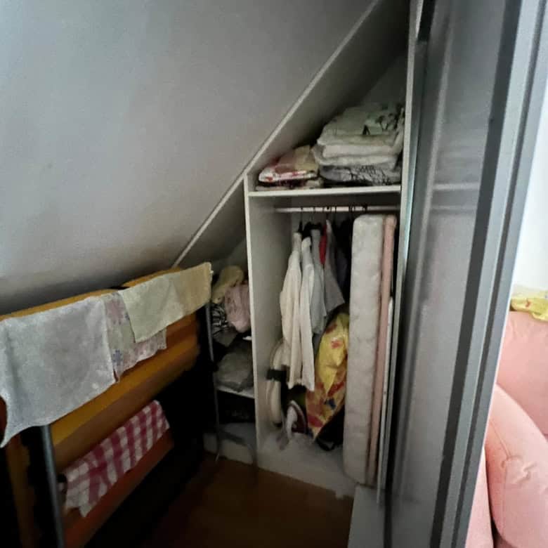 Built-in wardrobe with hanging clothes and shelves in a small bedroom.