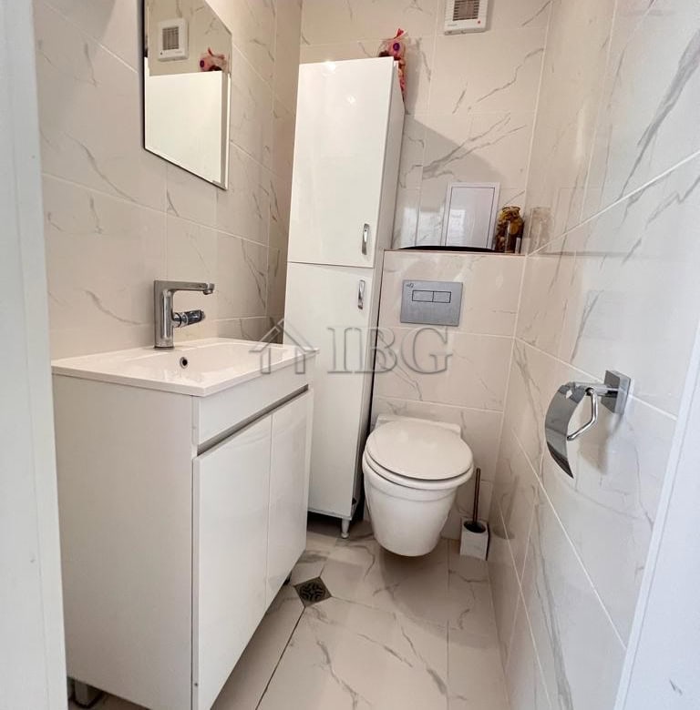 Bathroom with white vanity, toilet, and storage cabinet in a bright, clean space.