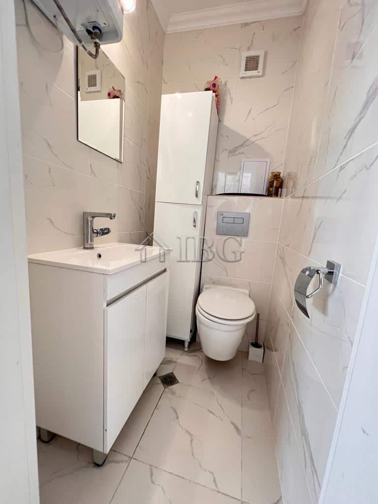 Bathroom with white vanity, toilet, and storage cabinet in a bright, clean space.
