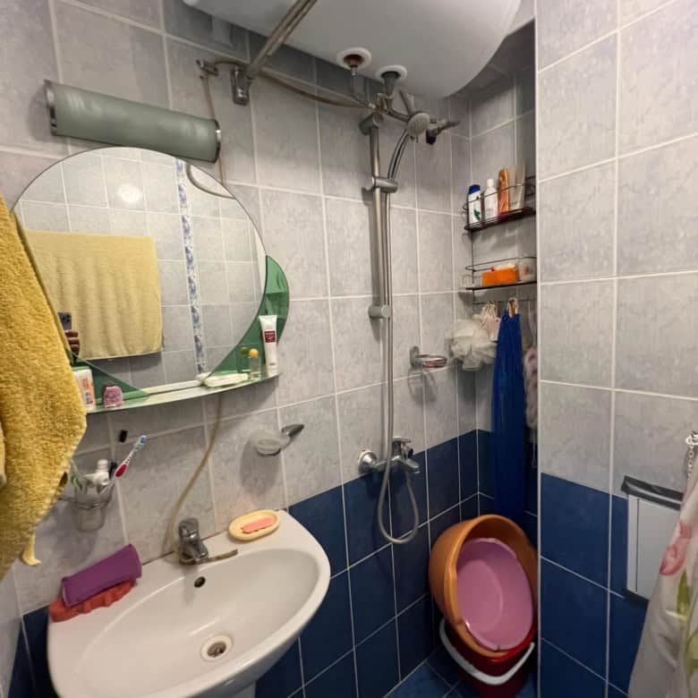Small bathroom with water heater, sink, mirror, and shower in a compact space.