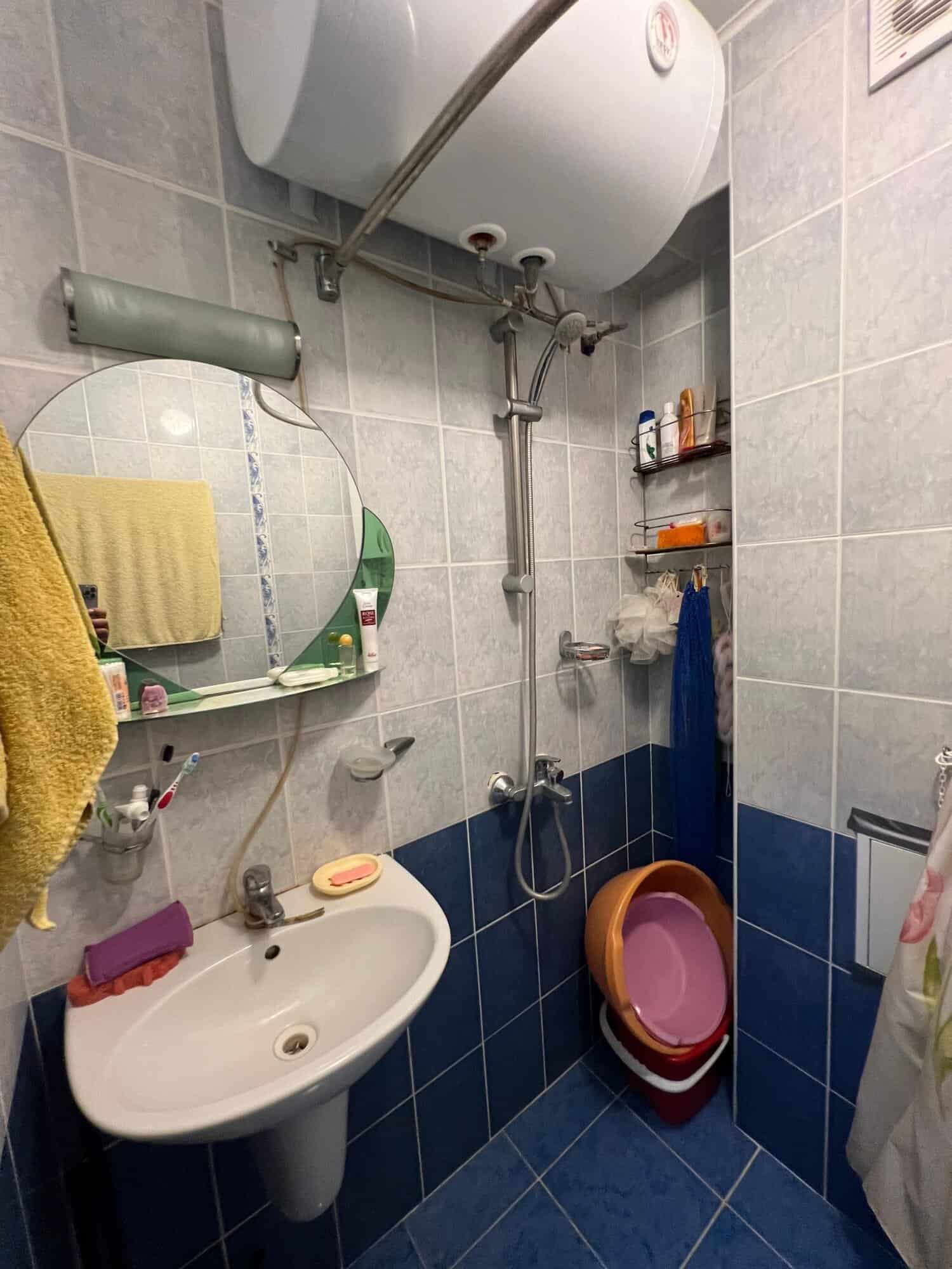 Small bathroom with water heater, sink, mirror, and shower in a compact space.