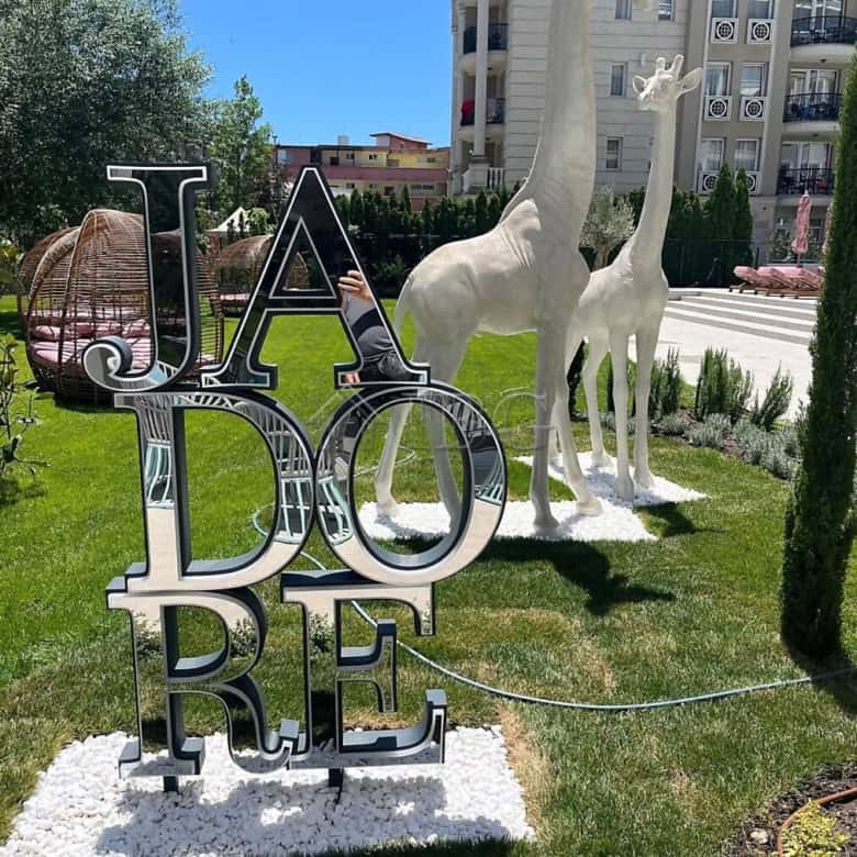 Modern outdoor sculpture with "J'adore" sign and giraffe statues in a landscaped garden.