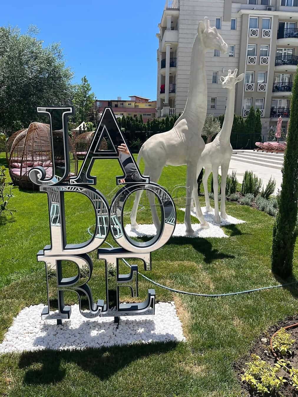 Modern outdoor sculpture with "J'adore" sign and giraffe statues in a landscaped garden.