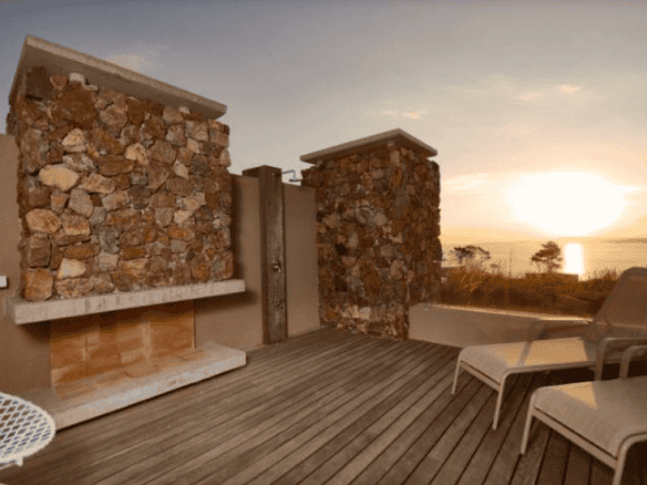 Terrace with stone walls and outdoor seating overlooking the ocean at sunset.