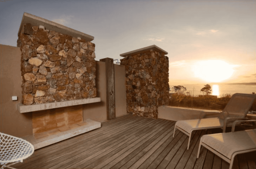 Terrace with stone walls and outdoor seating overlooking the ocean at sunset.