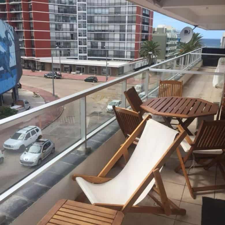 Balcony with wooden table, chairs, and sun lounger in a high-rise apartment in Punta del Este.