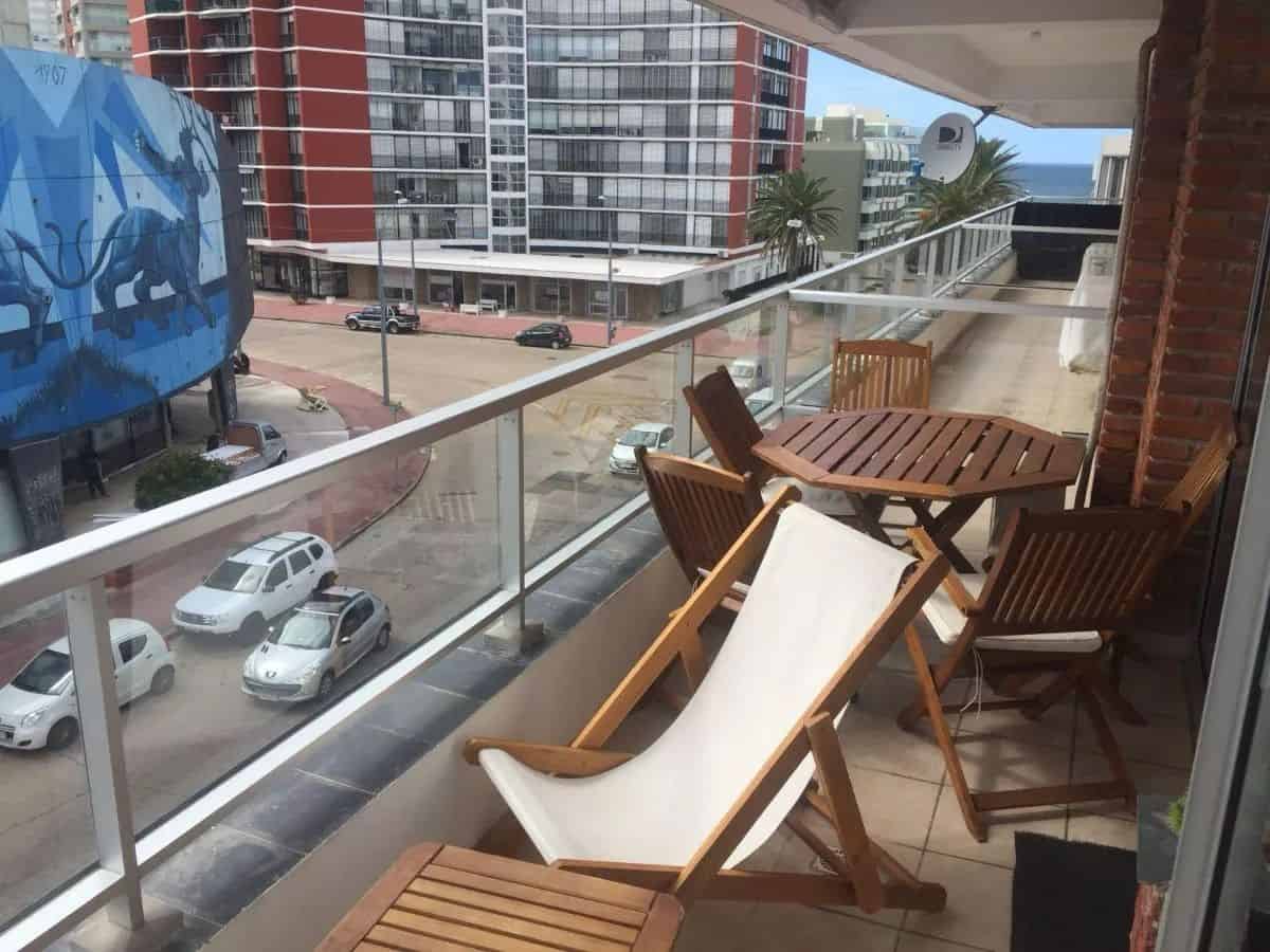 Balcony with wooden table, chairs, and sun lounger in a high-rise apartment in Punta del Este.