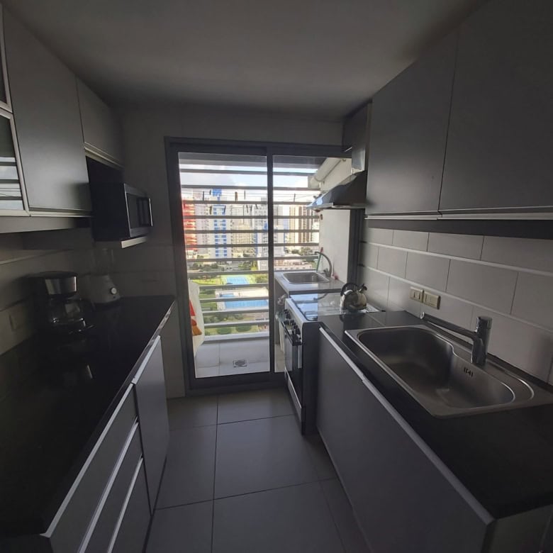 Modern kitchen with black countertops and stainless steel sink in Punta del Este apartment.