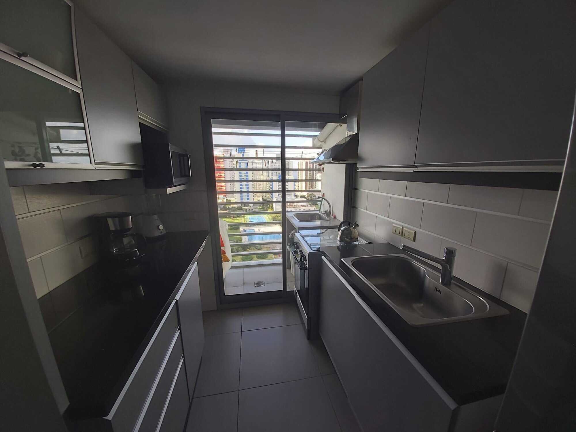 Modern kitchen with black countertops and stainless steel sink in Punta del Este apartment.