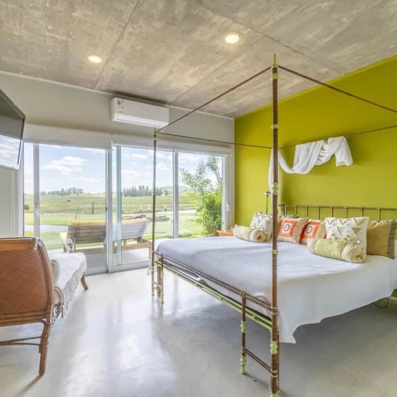 Modern bedroom with a green accent wall, large glass doors opening to a balcony with scenic countrys.