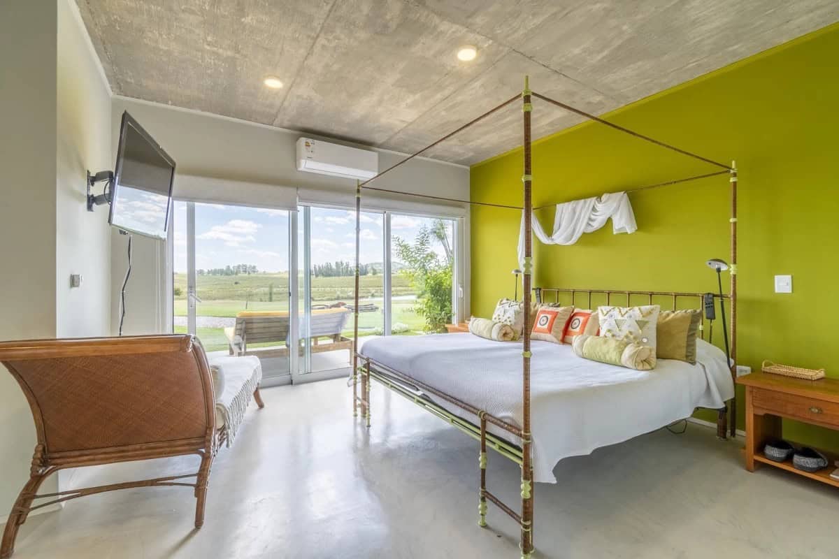 Modern bedroom with a green accent wall, large glass doors opening to a balcony with scenic countrys.