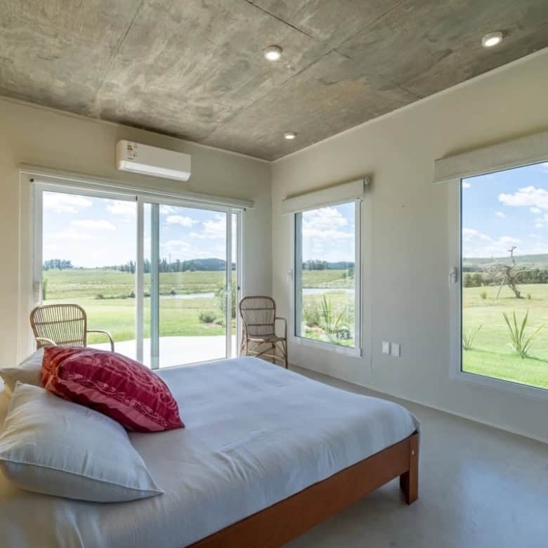 Beautiful bedroom with large windows overlooking lush green landscape in Punta Ballena. Modern inter.