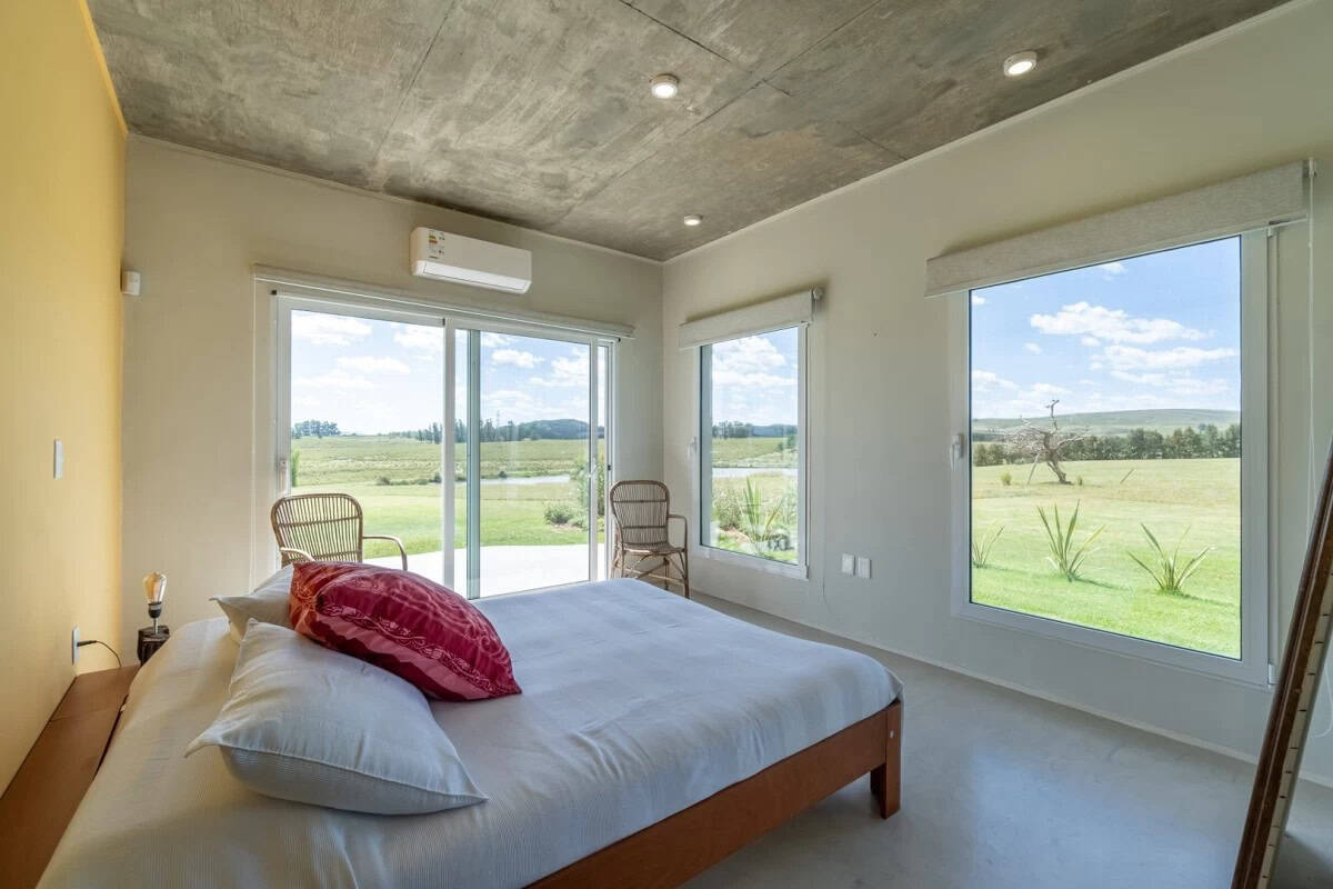 Beautiful bedroom with large windows overlooking lush green landscape in Punta Ballena. Modern inter.